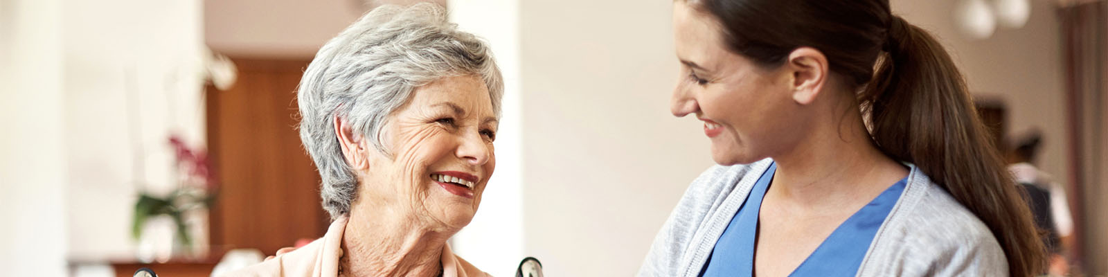 A senior woman sitting in a wheelchair looking over at her nursing assistant