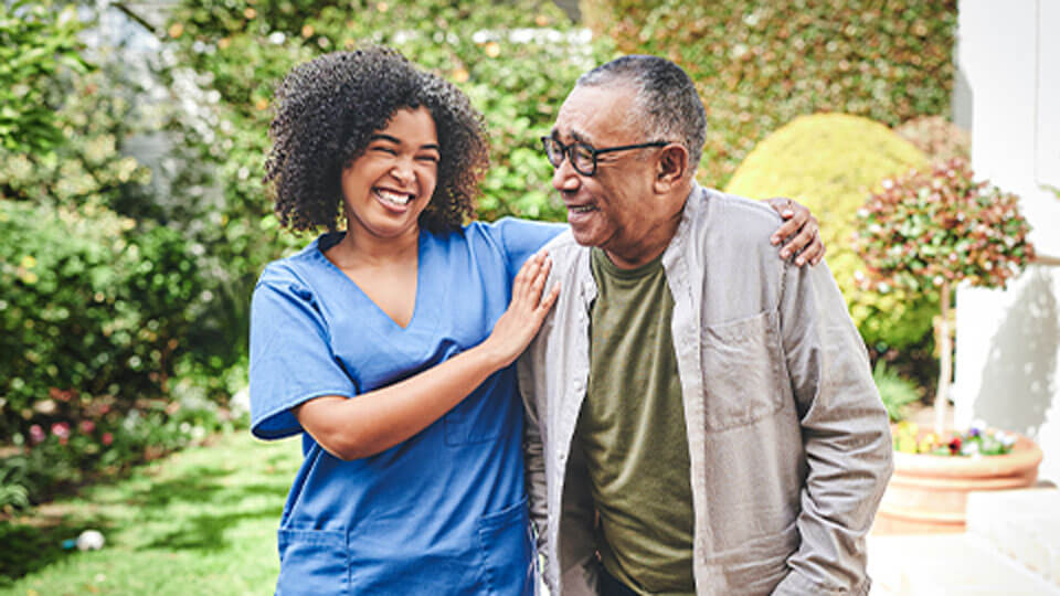 Male senior living resident walking outdoors as his caregiver helps to stabilize him at Traditions of Lafayette